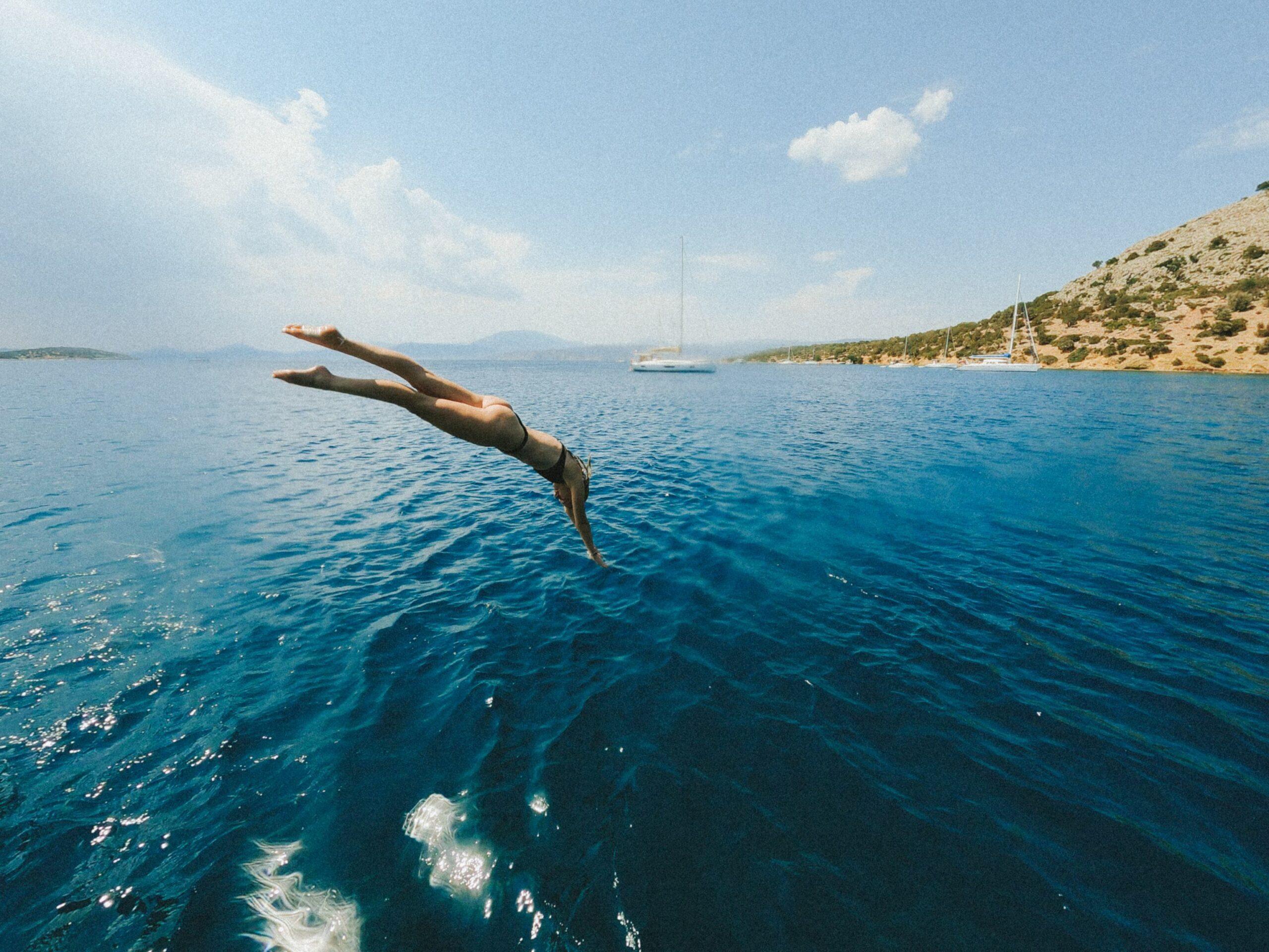 A sunlit outdoor photograph of guests enjoying a summer day aboard a sailboat on open turquoise waters during The Yacht Week.